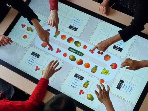 Plusieurs personnes participent ensemble à un jeu cognitif sur la grande table tactile interactive.